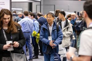 Diverse professionals networking at a busy conference expo hall, with attendees wearing lanyards and badges.