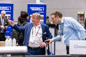 Two businessmen converse at a Northrop Grumman trade show booth during a professional conference.