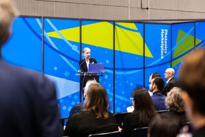 Speaker presents at Photonics Marketplace conference podium before seated audience with blue branded backdrop.