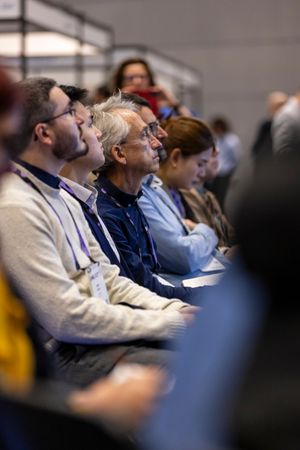 Engaged conference attendees with lanyards listen attentively during professional photonics industry presentation.