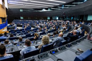 Large European Parliament chamber filled with delegates seated at blue chairs during an official plenary session.