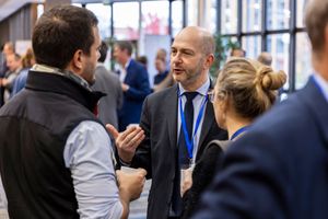 Business professionals networking at a conference event, engaged in conversation wearing suits and lanyards.