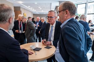 Business professionals in suits networking at a corporate event, gathered around a round table in a modern conference venue.