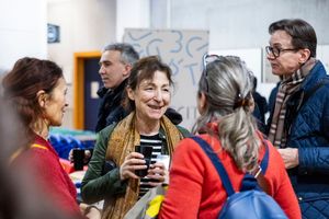 Group of older adults socializing at an indoor event, smiling and holding coffee cups in a casual gathering.