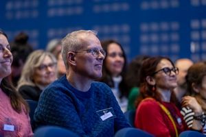 Audience members smiling and engaged during a conference presentation in a modern auditorium.