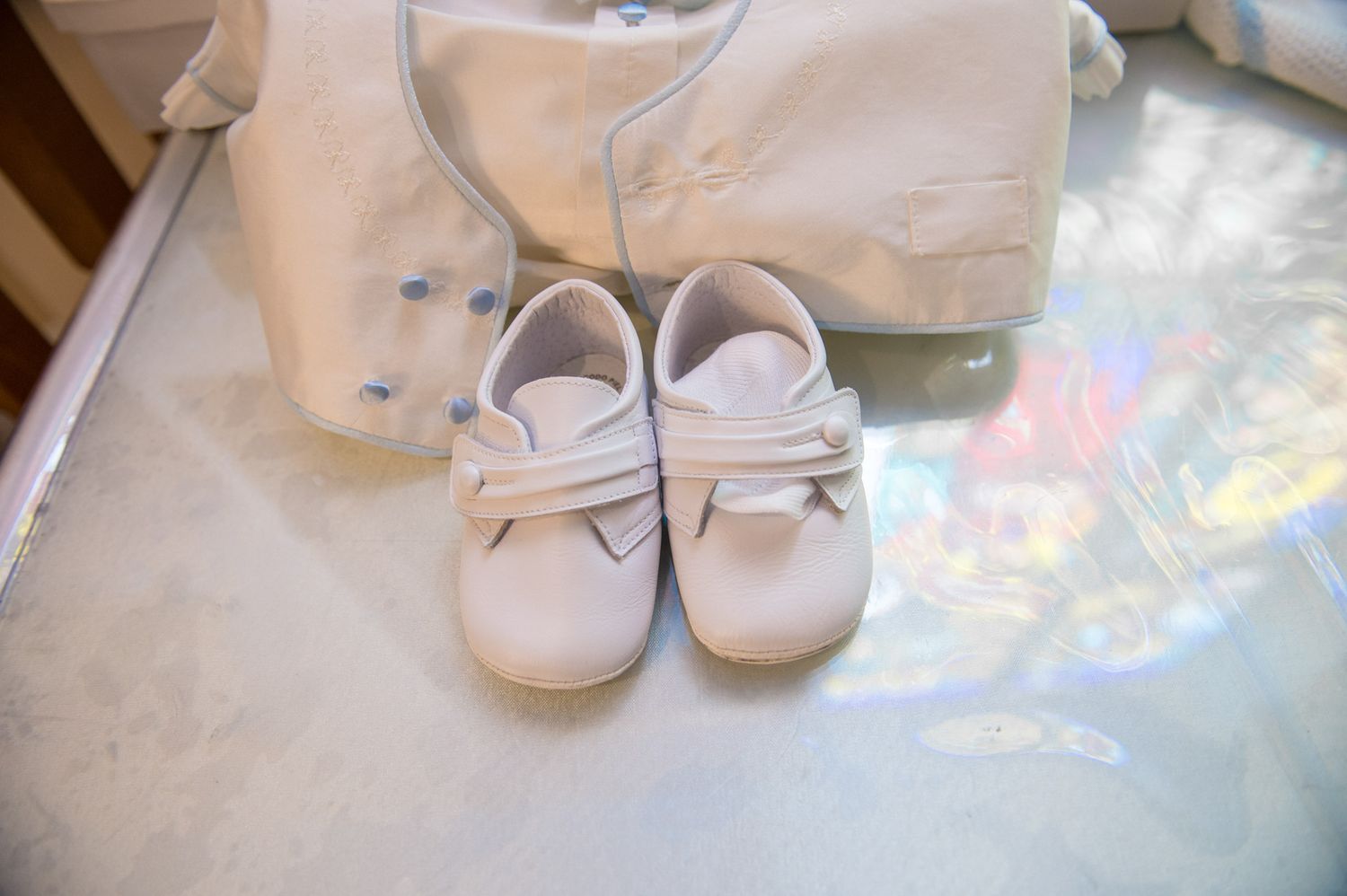 Small white leather baby shoes displayed on a reflective glass surface at a baptism ceremony.