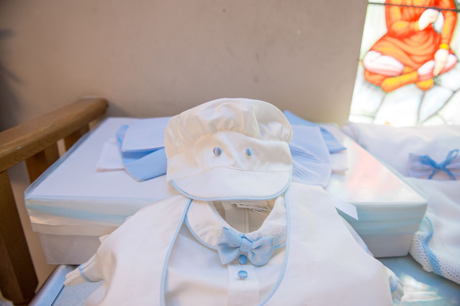 White baptism hat and outfit with blue bow tie neatly arranged on a table in a church setting.