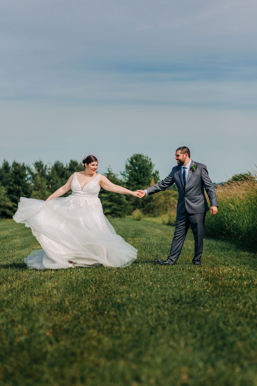 Candid wedding photo of groom twirling his bride in a field during their summer wedding near woodstock, ontario.