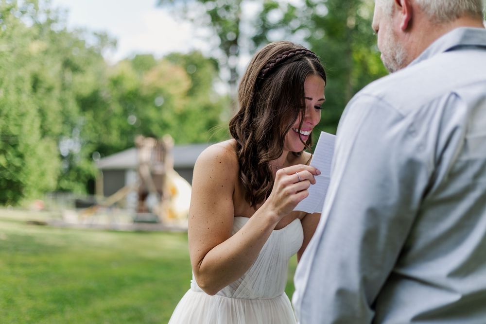 Candid wedding photo of bride laughing while reading vows during their backyard summer wedding near woodstock, ontario.
