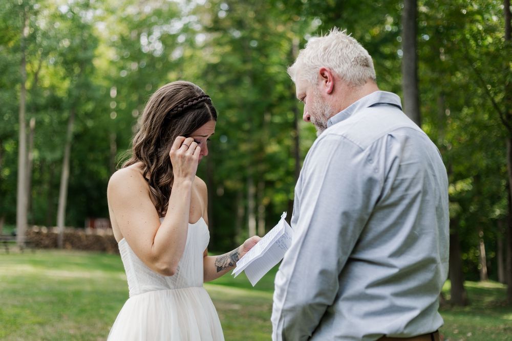 Candid wedding photo of bride crying while reading her private vows surrounded by greenery near woodstock, ontario.