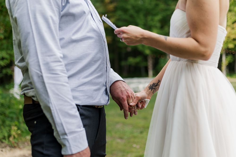 Close up of bride and groom holding hands during a private vow reading during their backyard summer wedding near woodstock, ontario.