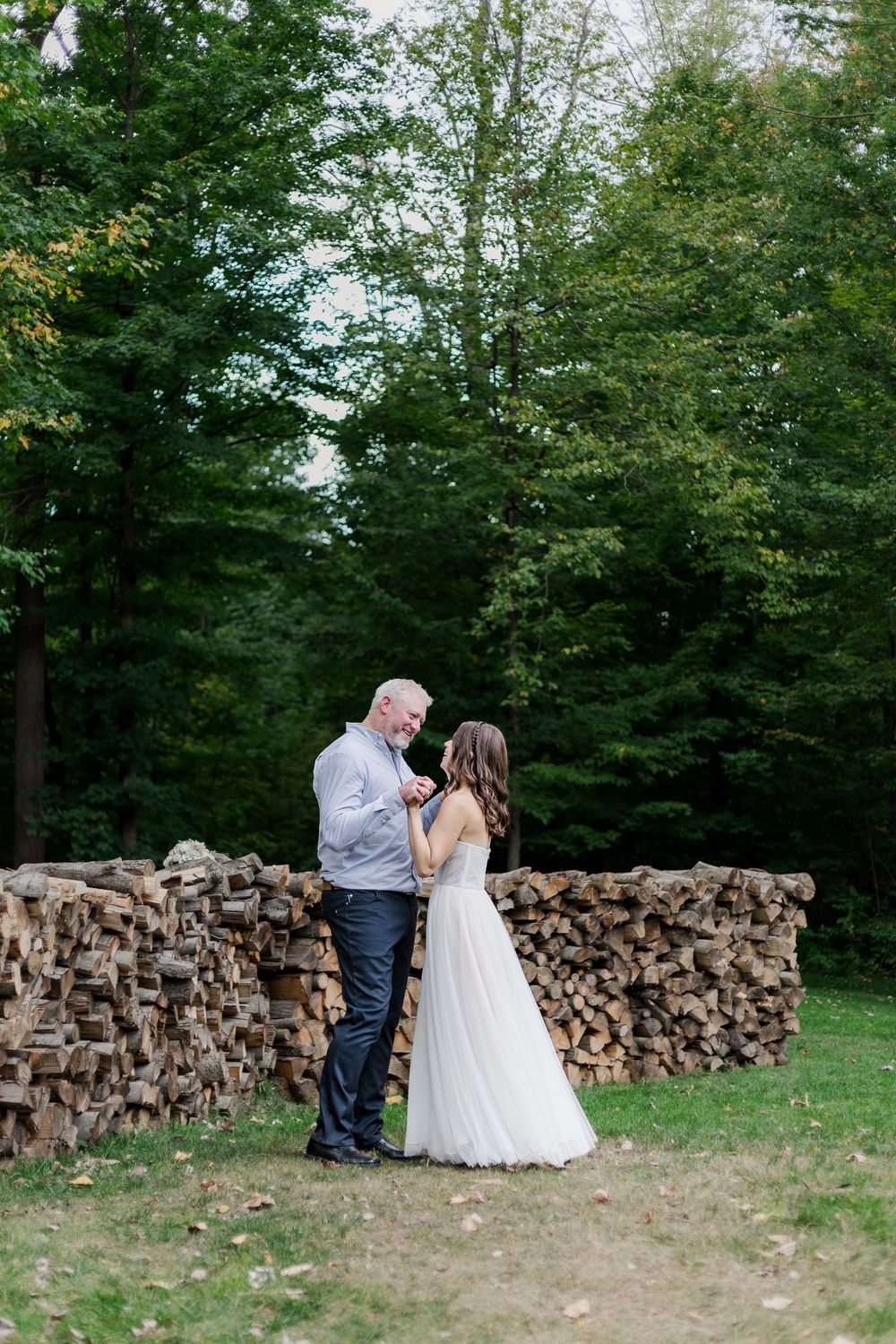 Bride and groom stand together in front of a pile of wood during their backyard wedding photos near woodstock, ontario.
