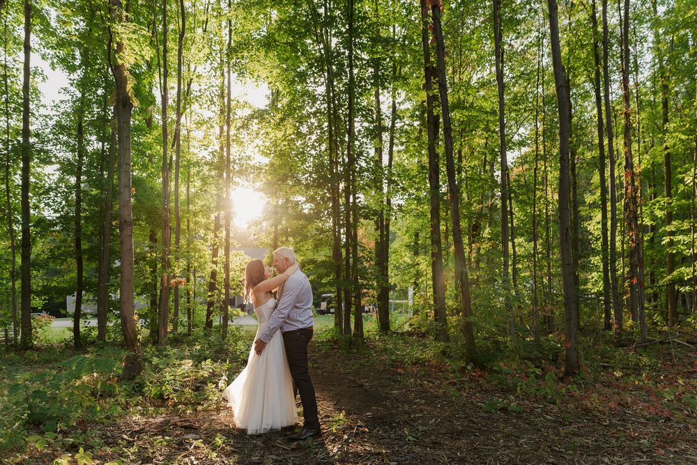 Bride and groom embrace each other surrounded by tall trees during sunset at their backyard summer wedding near woodstock, ontario.