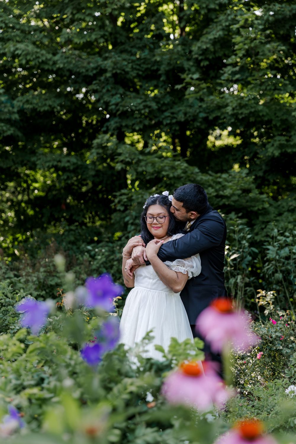 Groom snuggles his bride surrounded by a lush garden for a natural wedding photo moment near woodstock, ontario.