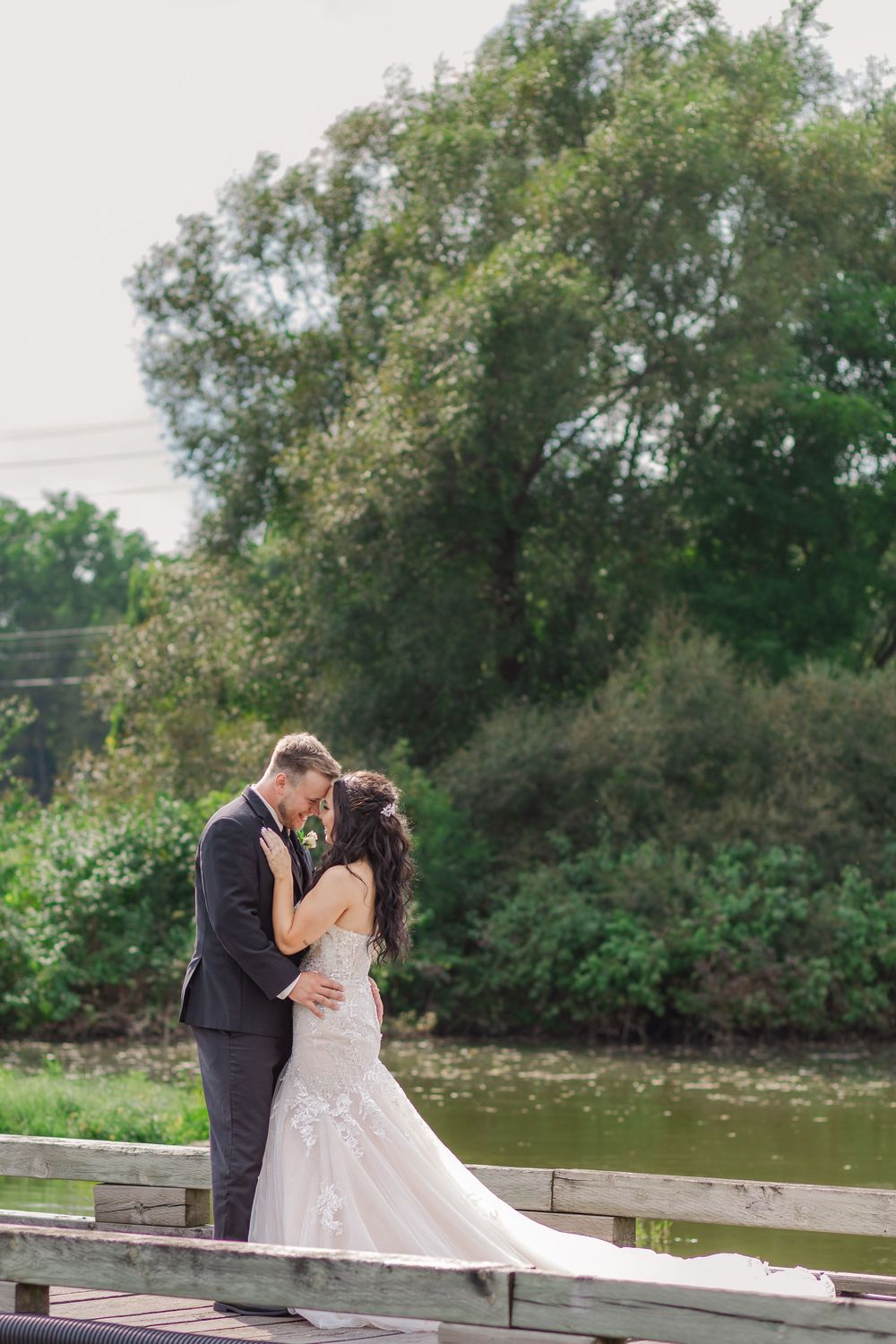 Bride and groom stand together on a wooden bridge near the water on a sunny summer wedding day near woodstock, ontario,