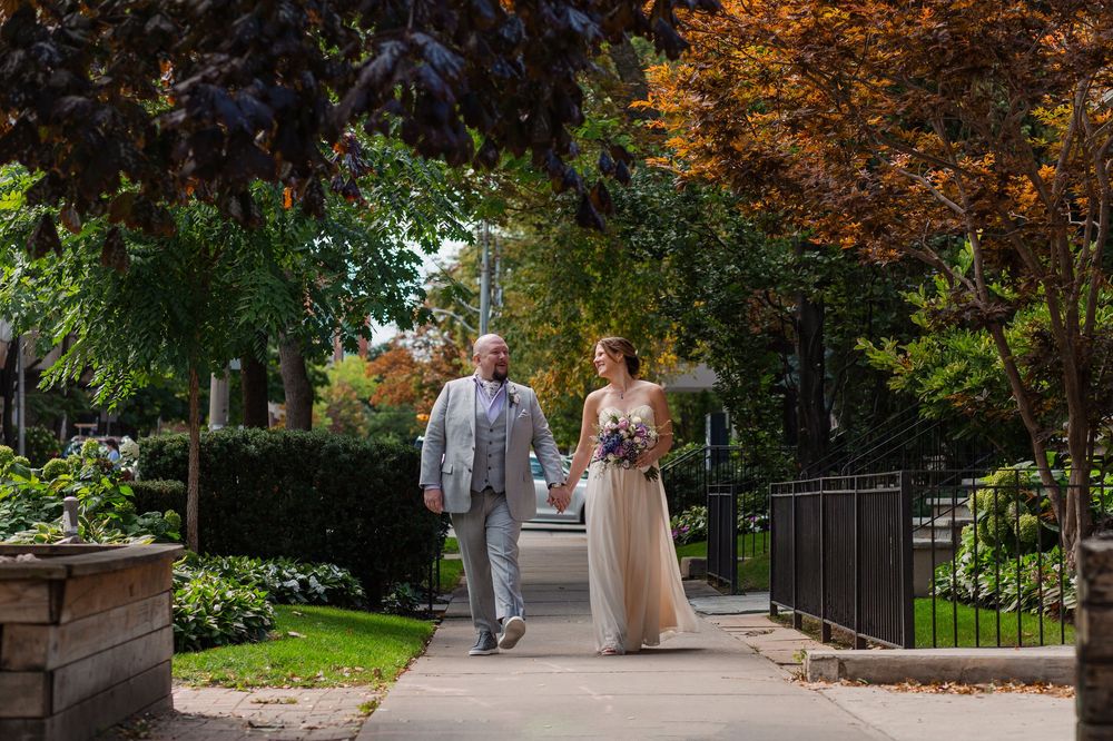 Candid wedding photo of bride and groom walking down the street during fall surrounded by colourful leaves near woodstock, ontario.