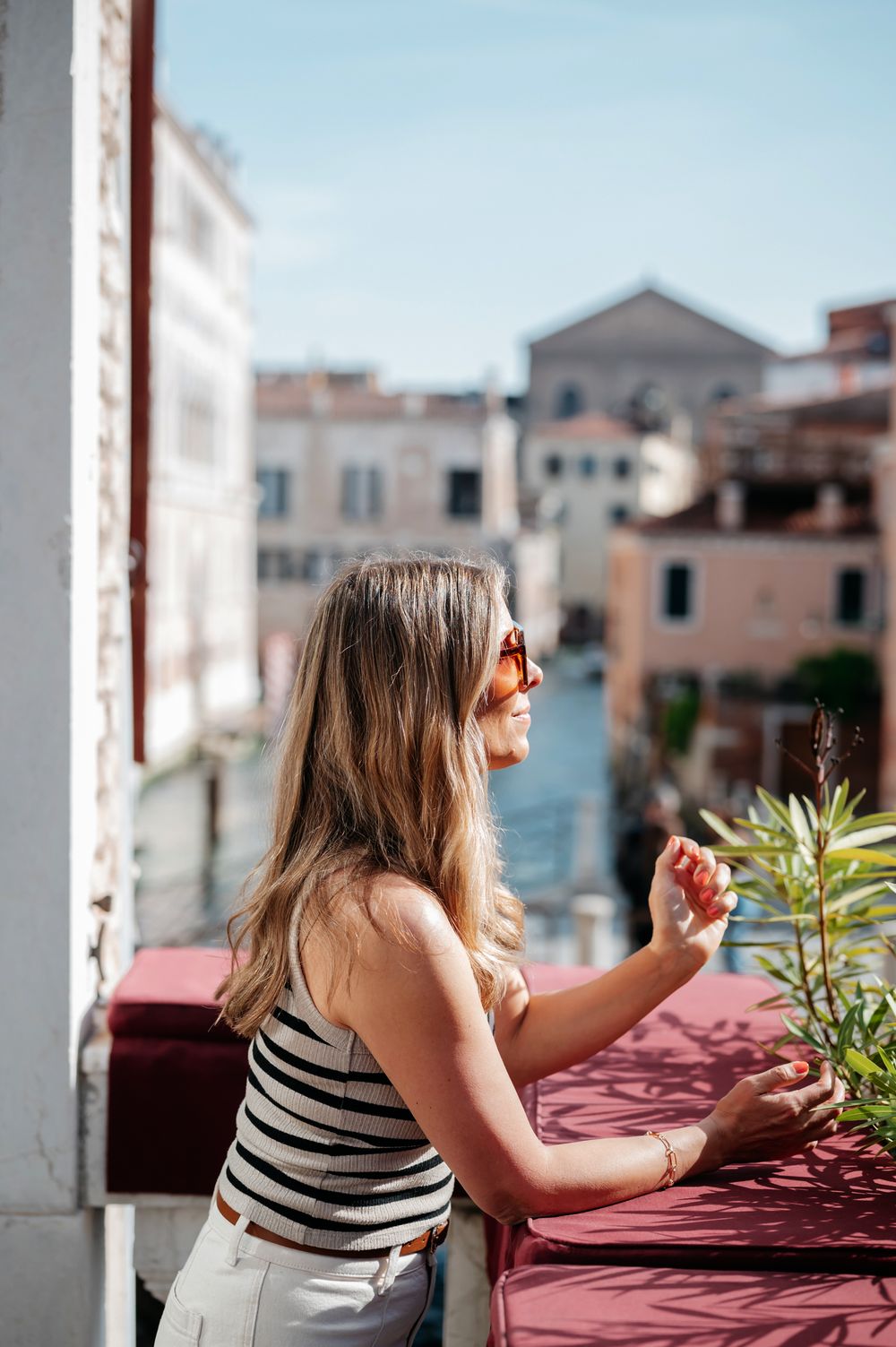 Woman in striped top and sunglasses enjoying a sunny balcony view of a European canal city.