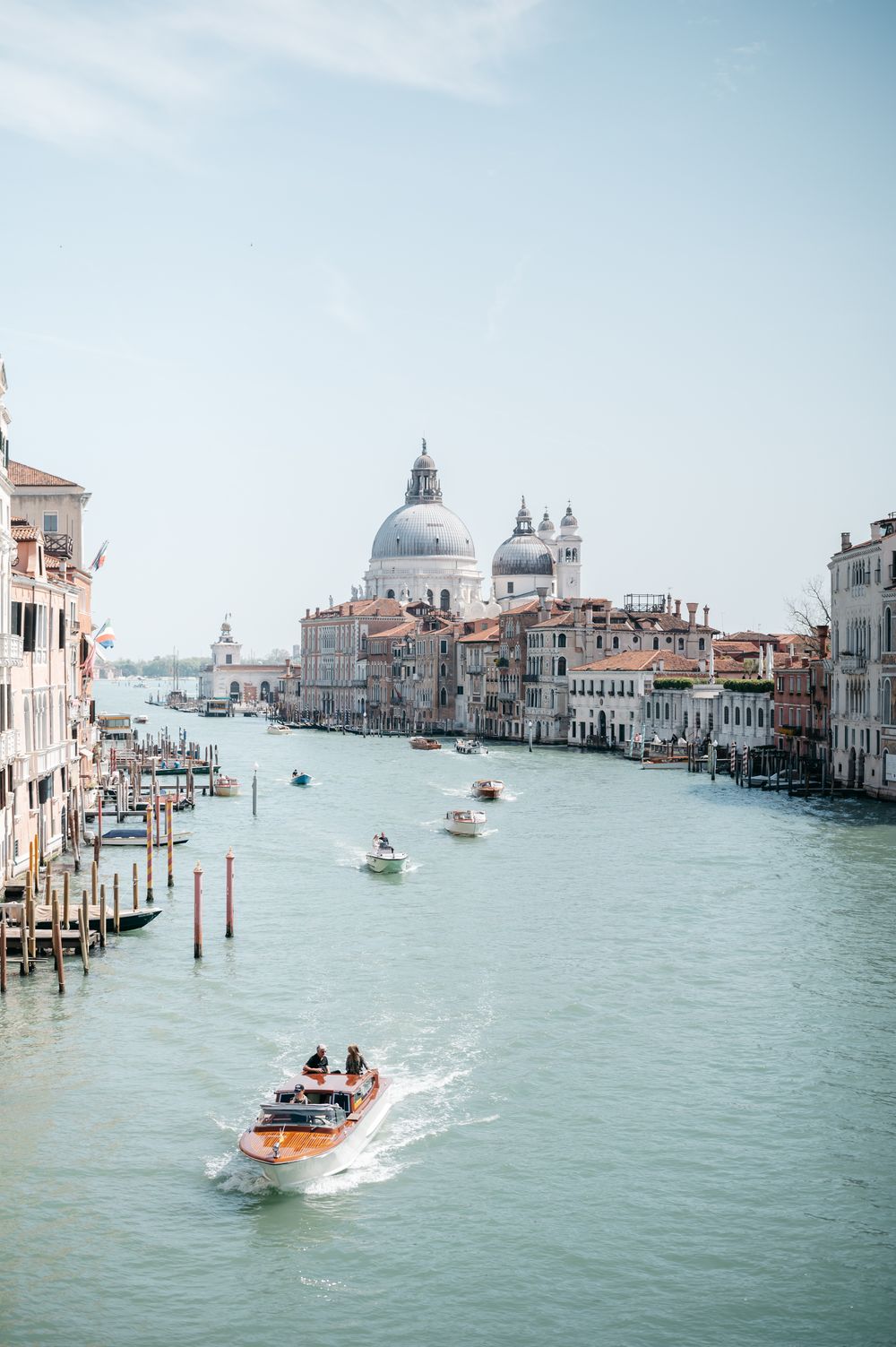 Boats navigate the Grand Canal in Venice, Italy, with the iconic Santa Maria della Salute basilica dome in the background.
