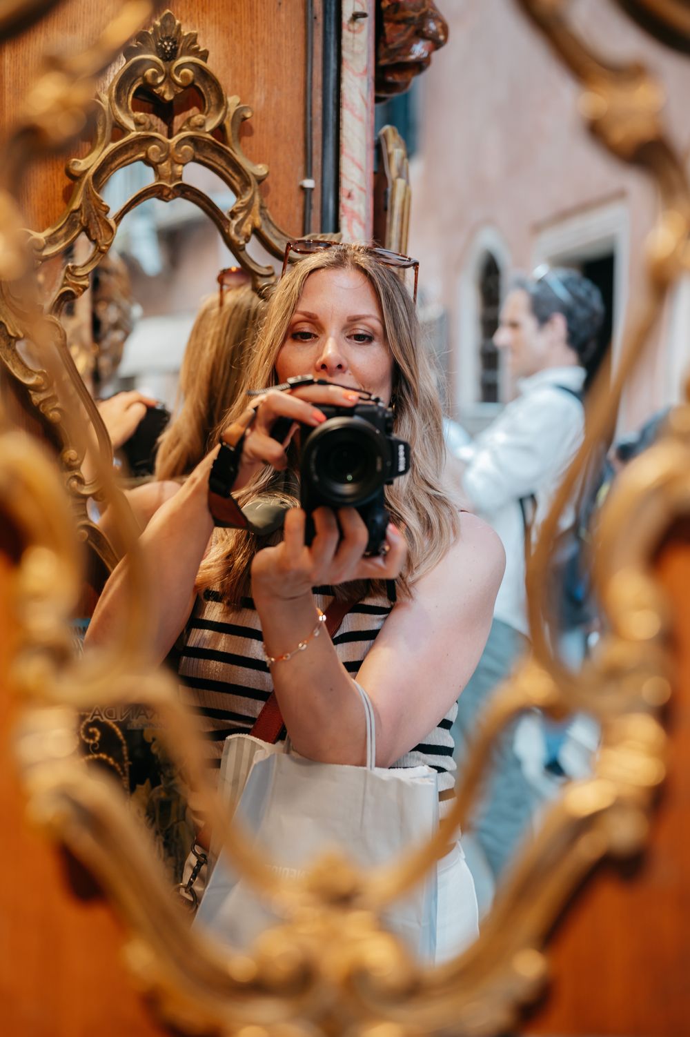 Woman taking mirror selfie with DSLR camera in ornate gold antique frame in Venice Italy.