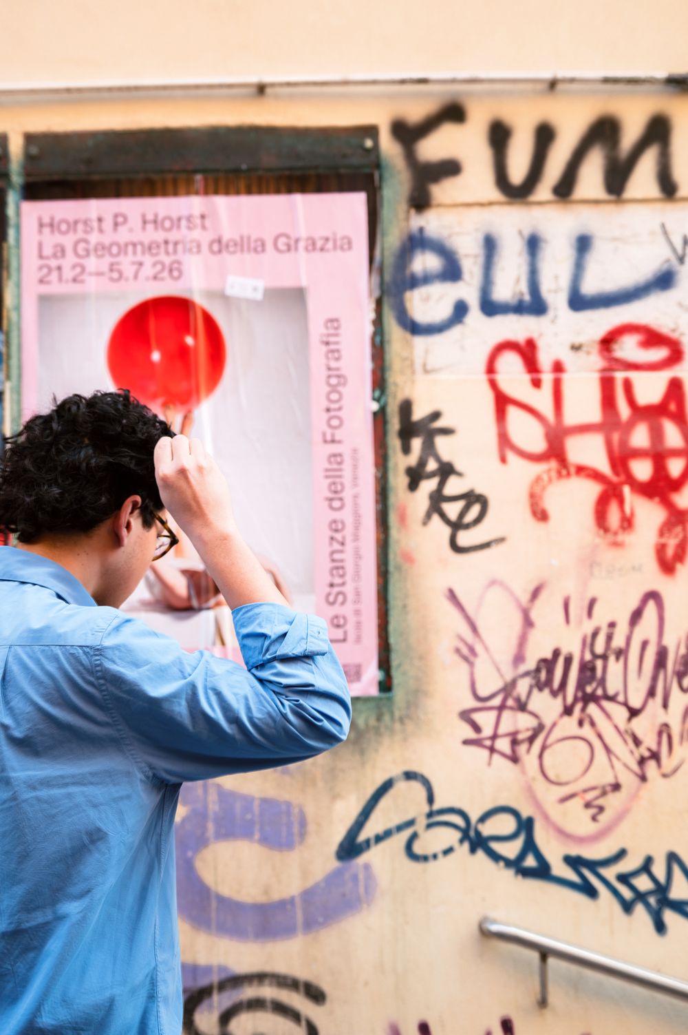 Man in blue shirt photographing a Horst P. Horst exhibition poster on a graffiti-covered wall in Venice.