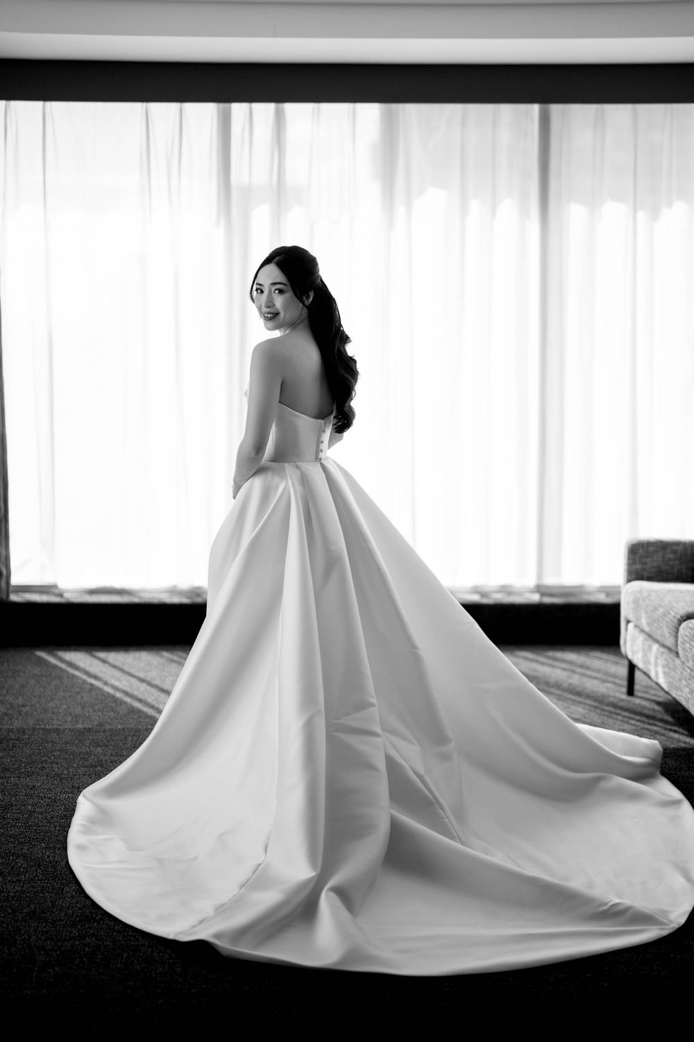 Stunning black and white portrait of Asian bride in strapless ballgown with dramatic train by window.