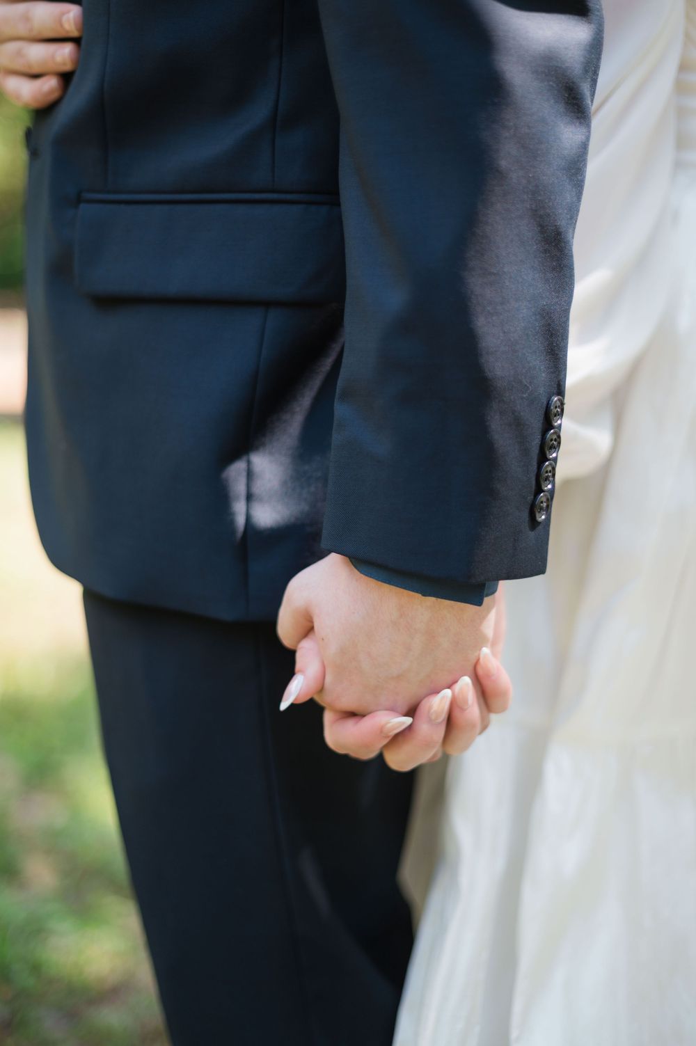 Close-up of bride and groom holding hands, showcasing wedding attire with navy suit and white bridal gown.
