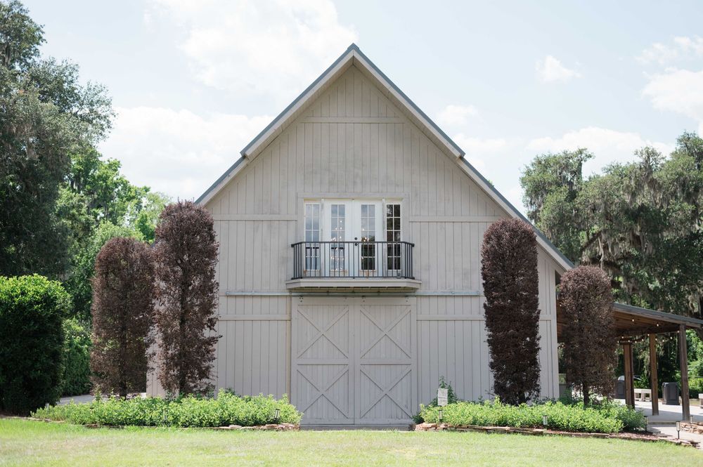 A charming white barn-style building with French balcony doors, flanked by dark trees on a sunny day.