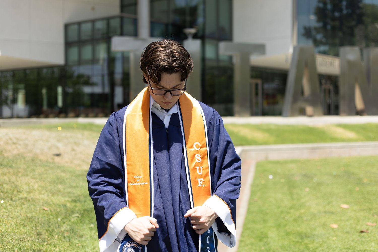 Cal State Fullerton Titan graduate looking at their cap and gown during a photo session. The words Titans in the background.
