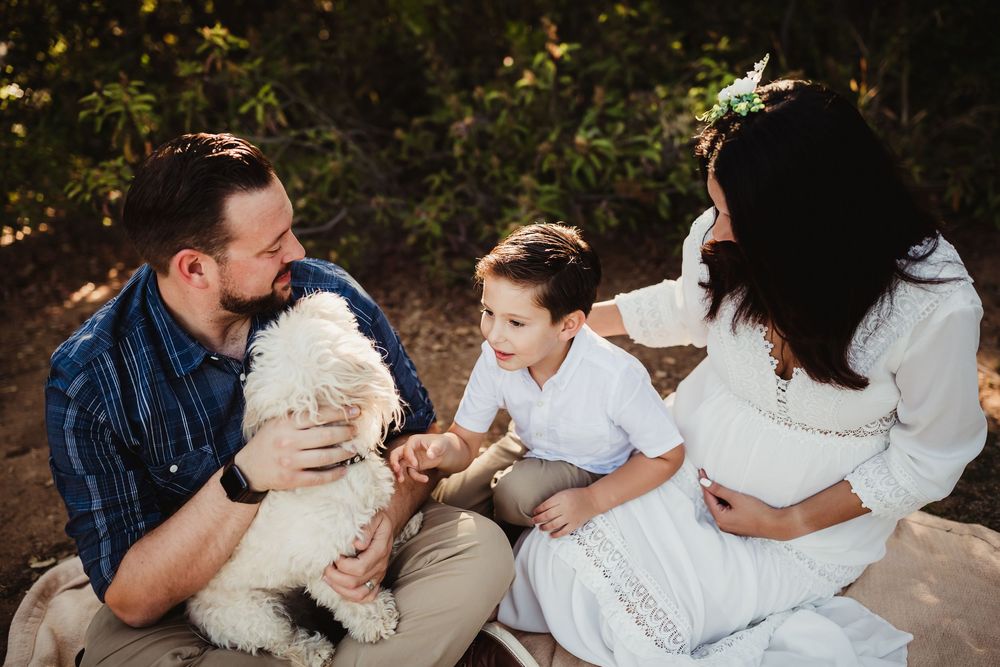 Family with a boy and white fluffy dog sitting outdoors for a maternity photo session in redlands ca