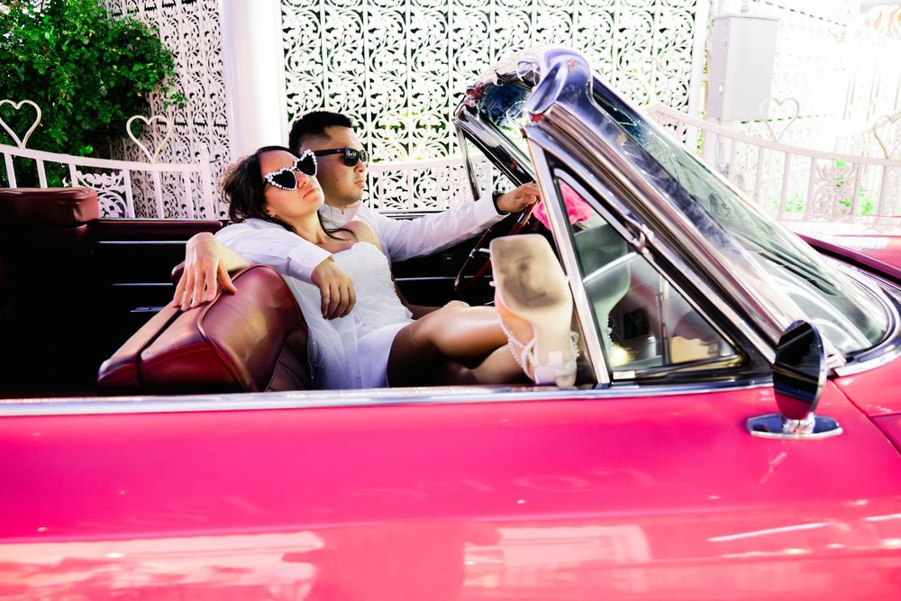 Stylish couple in sunglasses relax together in a vintage pink convertible car outdoors.