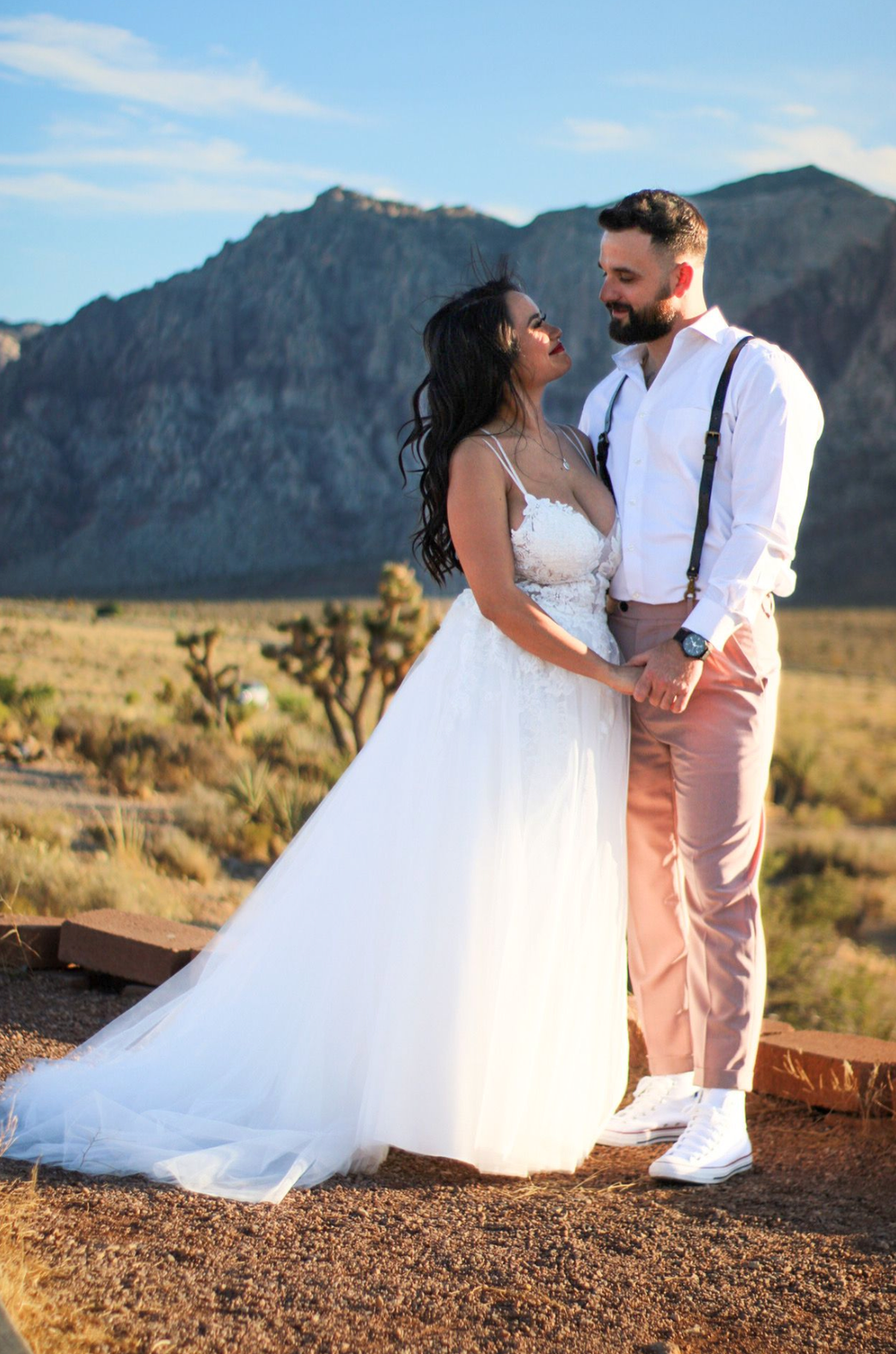 Bride and groom share romantic moment in desert landscape with mountain backdrop at golden hour.