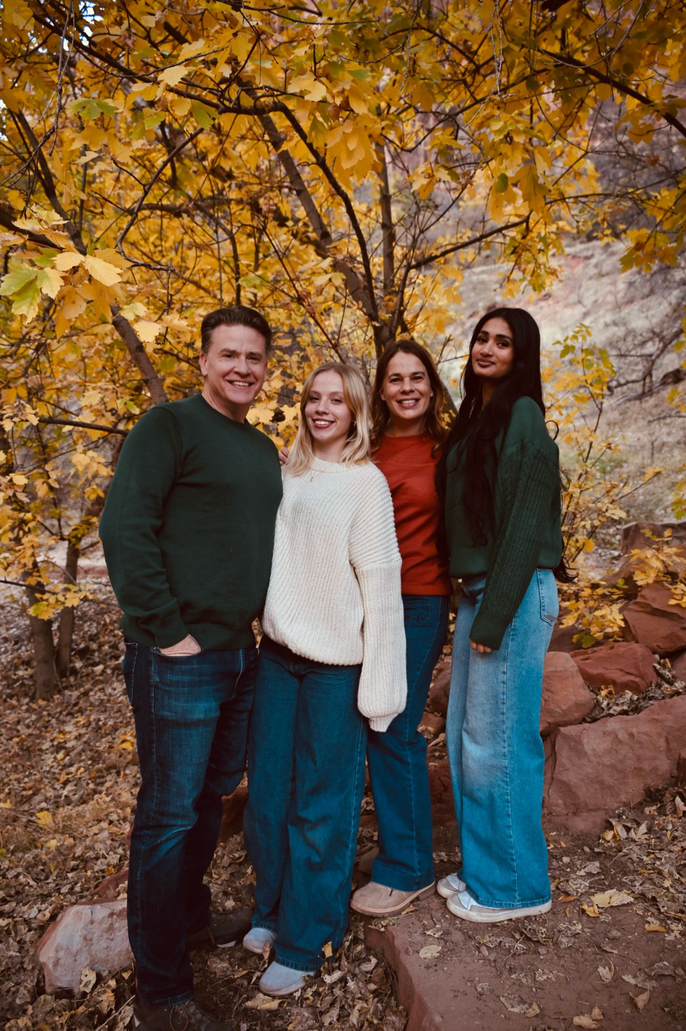 Happy family of four poses together under golden autumn foliage in a canyon setting.