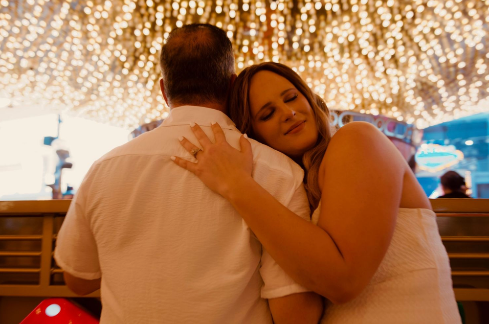 Couple sharing a romantic embrace under twinkling fairy lights at a Disney-themed venue.