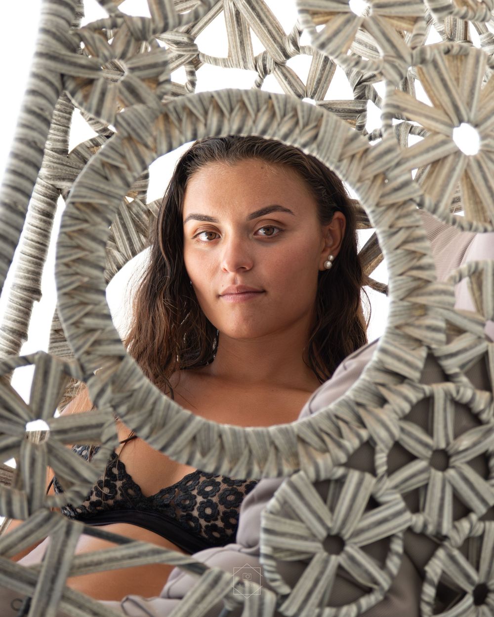 Young woman with dark hair and pearl earring reflected in a decorative woven mirror frame.