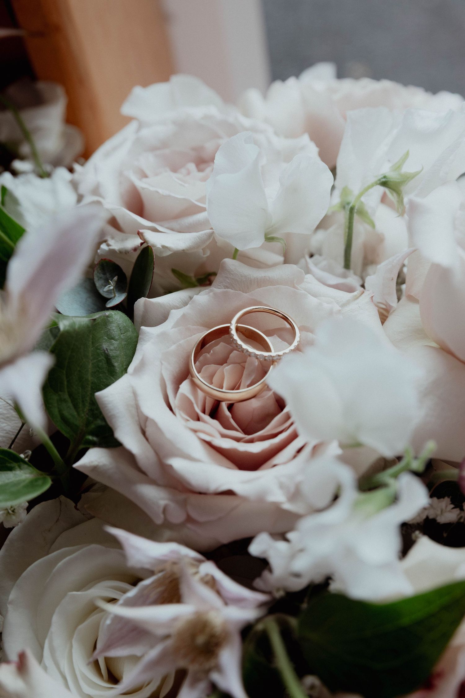 Two gold wedding rings resting elegantly on a bouquet of soft pink and white roses.