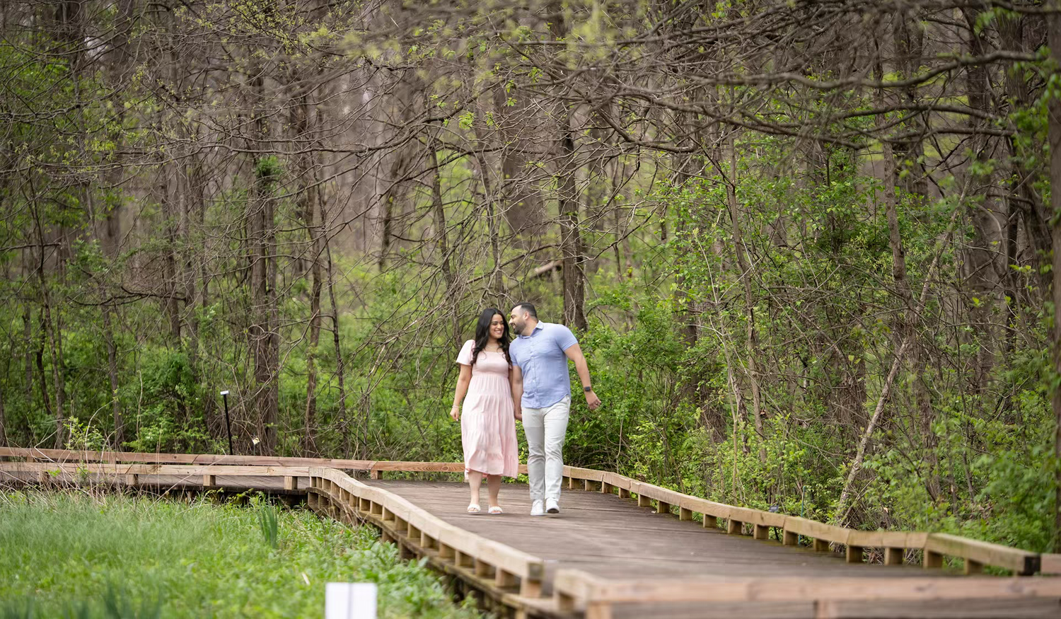 engagement session of Couple walking hand-in-hand on a wooden boardwalk path at Inniswood Metro Gardens
