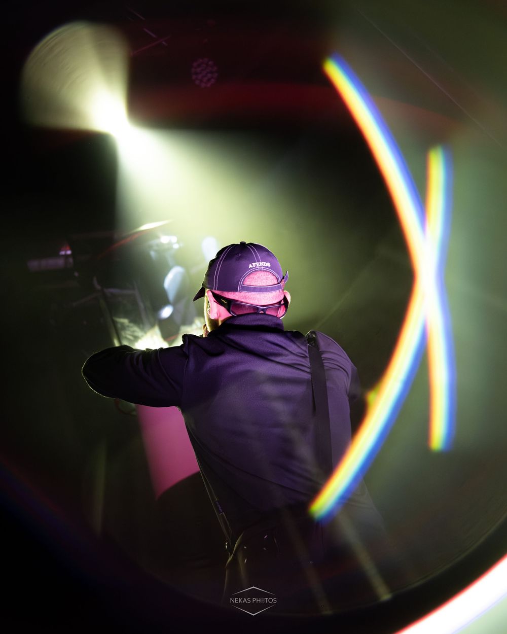 Musician performing on stage with dramatic rainbow lens flare light effects and spotlight in dark concert venue.