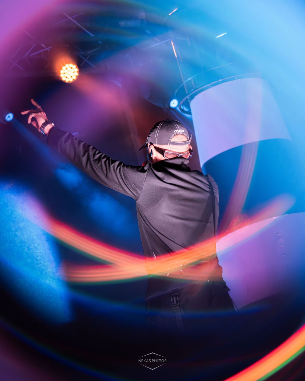 DJ performing energetically on stage with colorful light trails and vibrant blue and purple stage lighting.