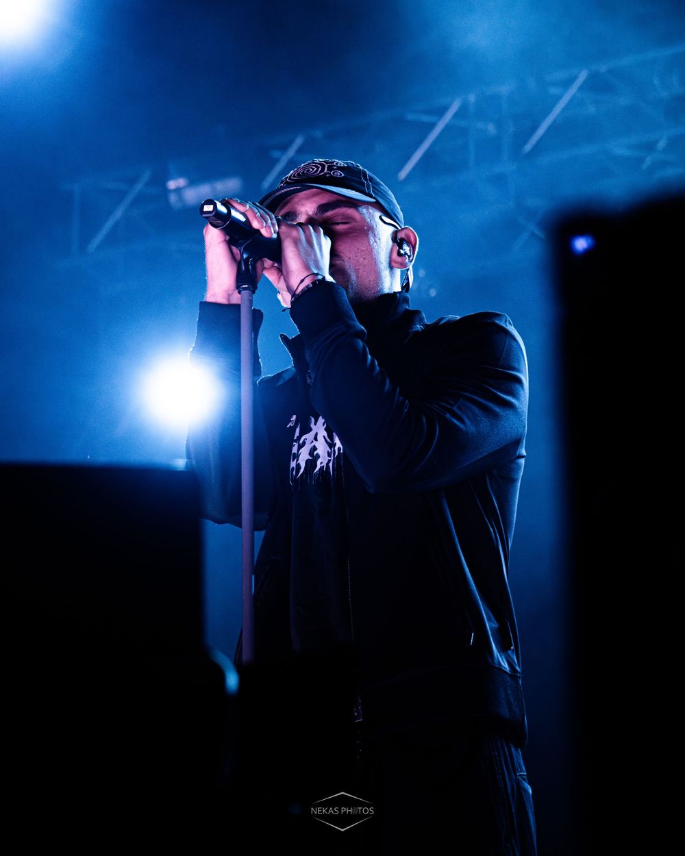 Male vocalist performs on stage holding microphone under dramatic blue stage lighting at a live concert.