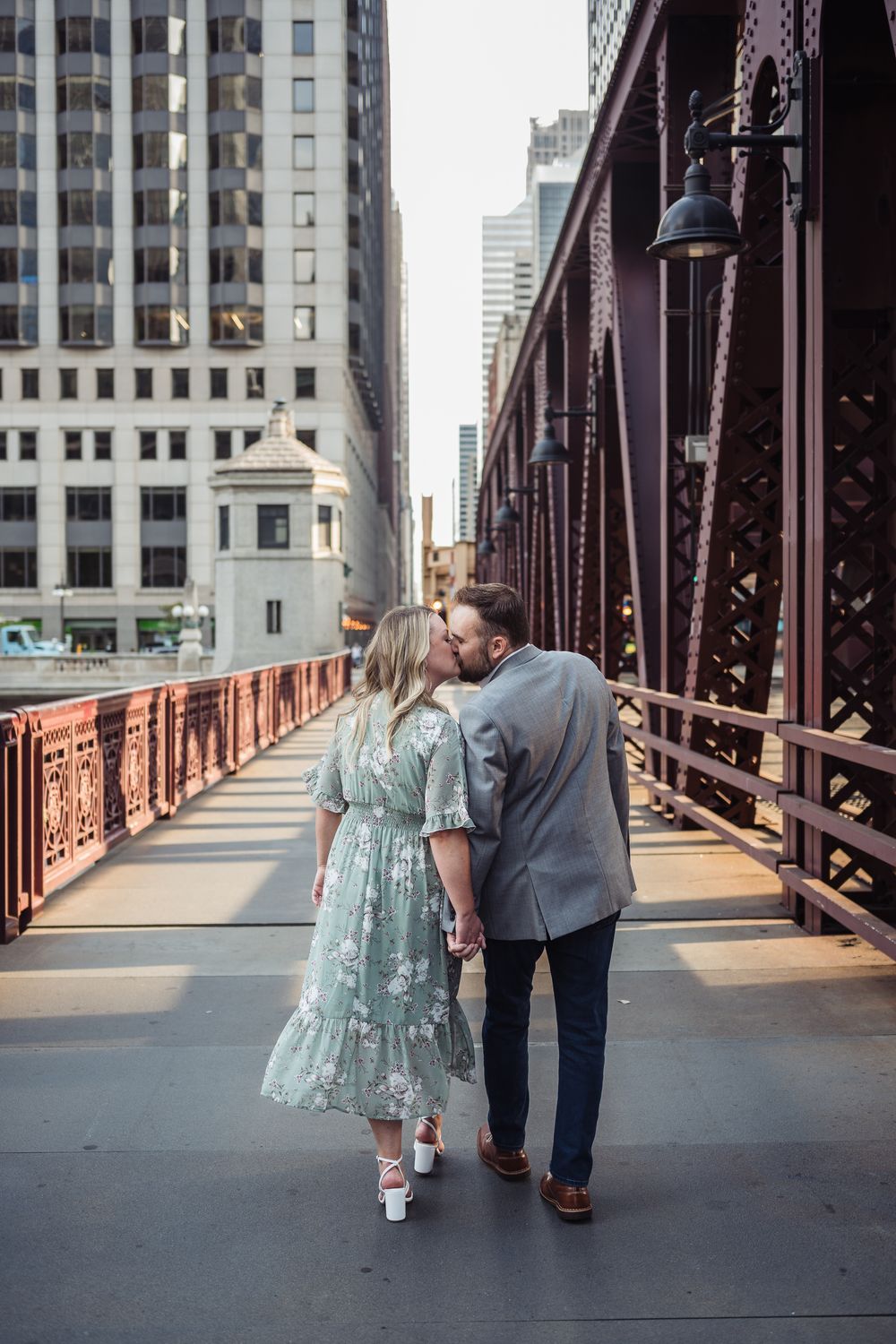 Couple kissing while holding hands on a historic iron bridge in downtown Chicago, woman in floral dress.
