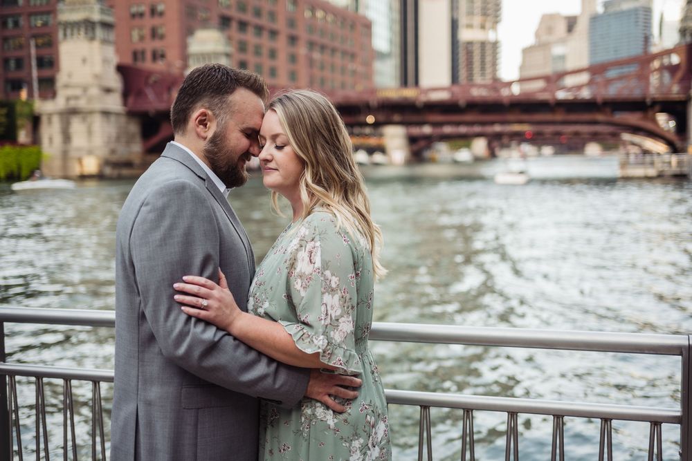 Couple embracing romantically on a bridge over the Chicago River, man in gray suit, woman in floral green dress.