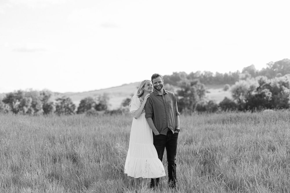 Black and white portrait of a couple embracing in a scenic grassy meadow.