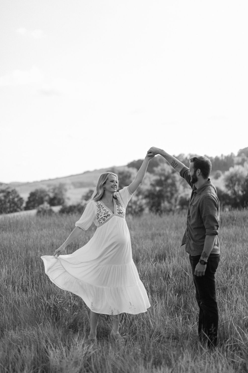 Black and white photo of a couple dancing in a grassy meadow under open sky.