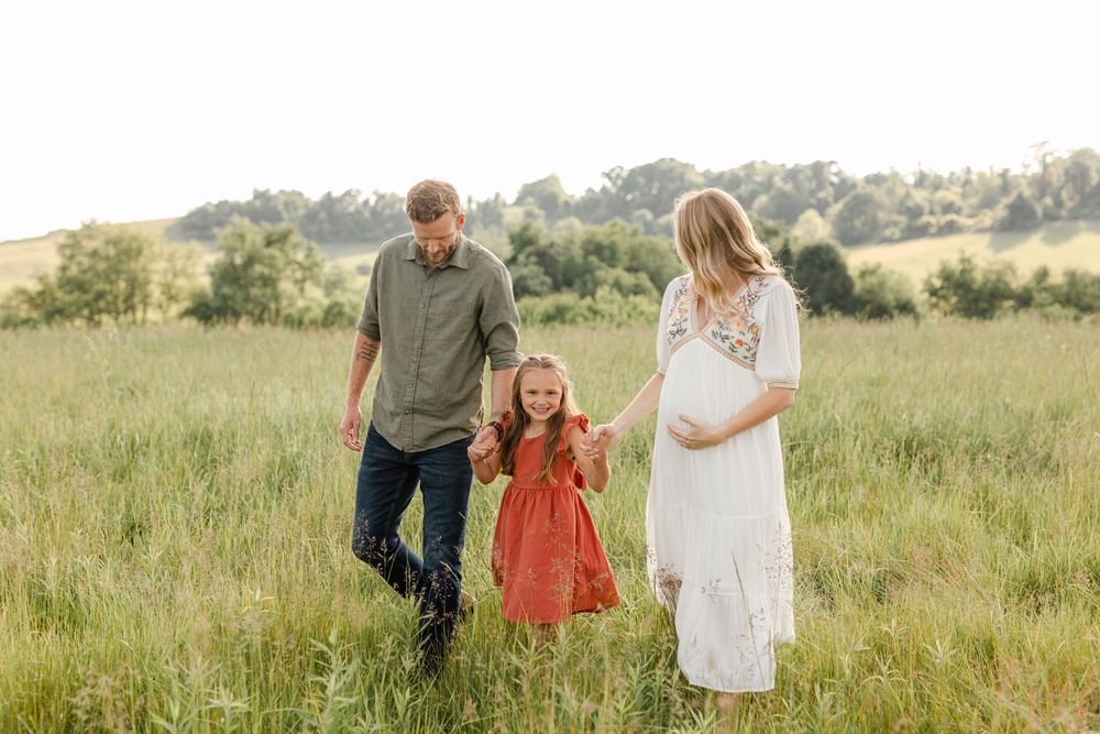 Family of three walking hand in hand through a lush green meadow together.