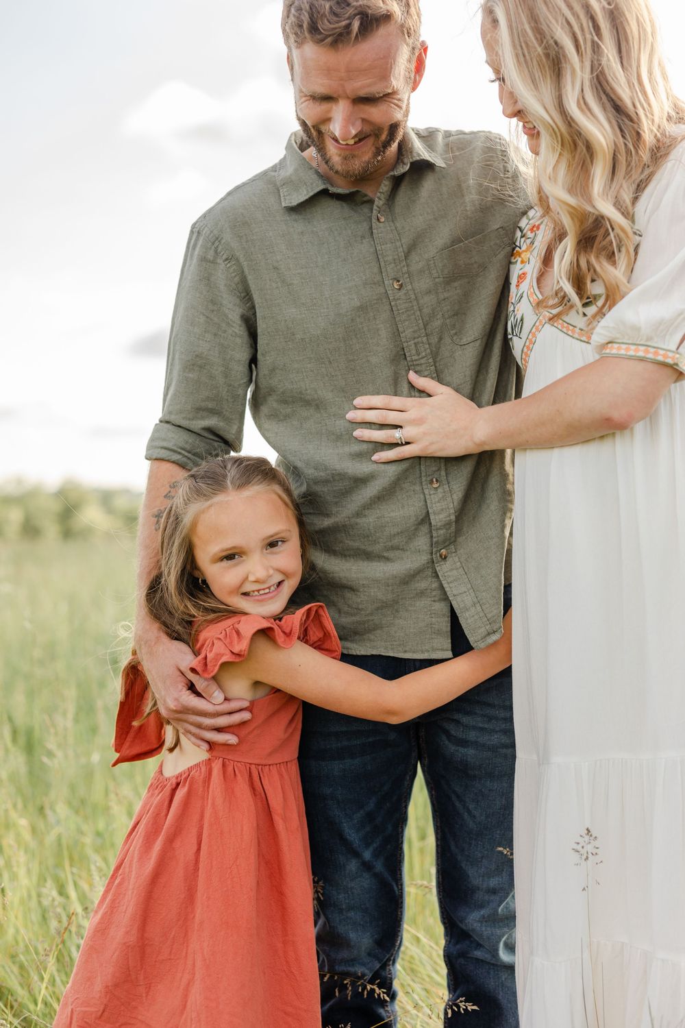 Smiling father and daughter in red dress hugging outdoors in a grassy field.