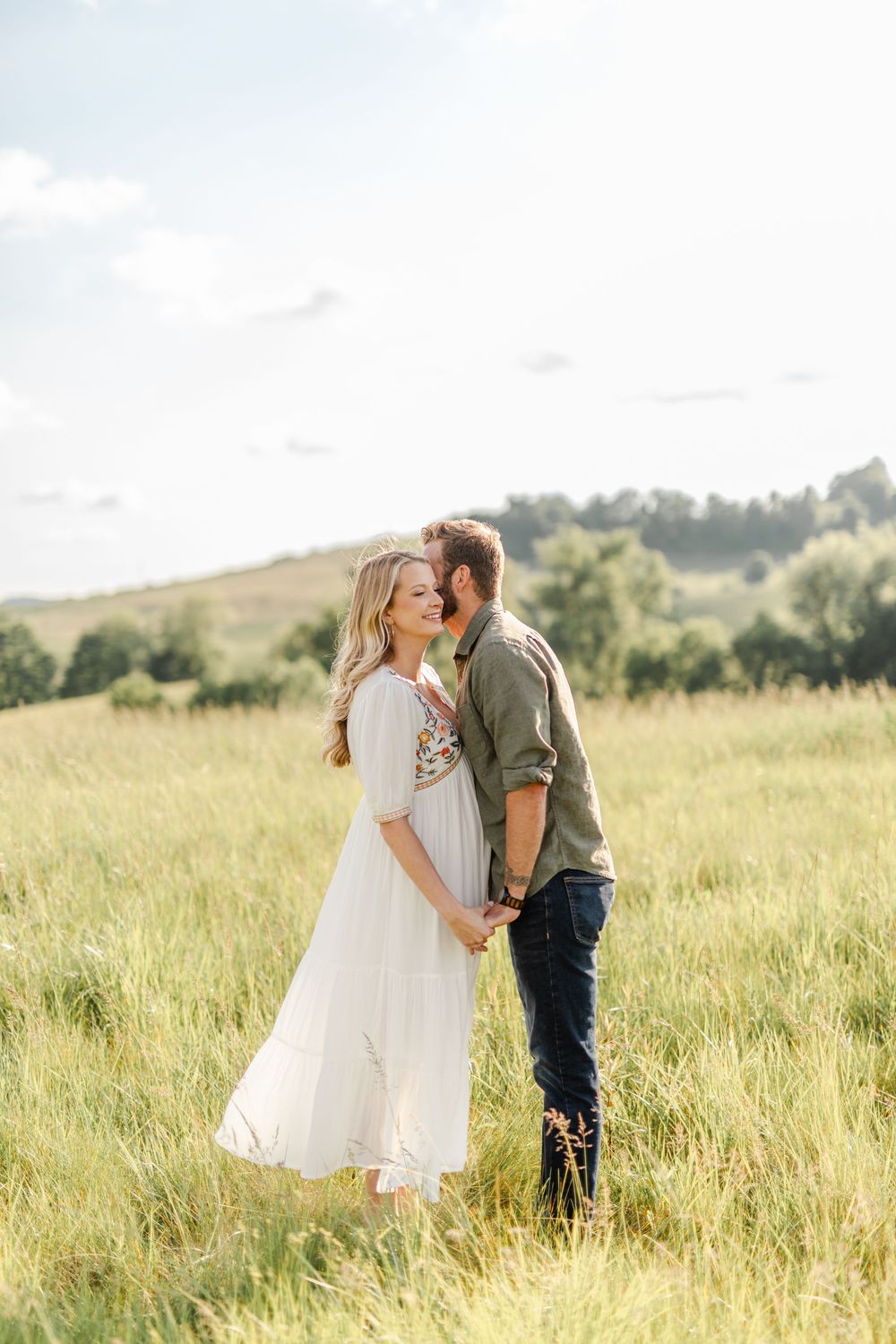 Romantic couple holding hands and gazing at each other in a sunny green meadow.