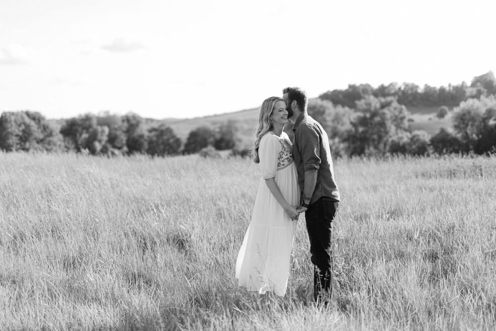 Black and white photo of a couple sharing a tender kiss in a grassy field.