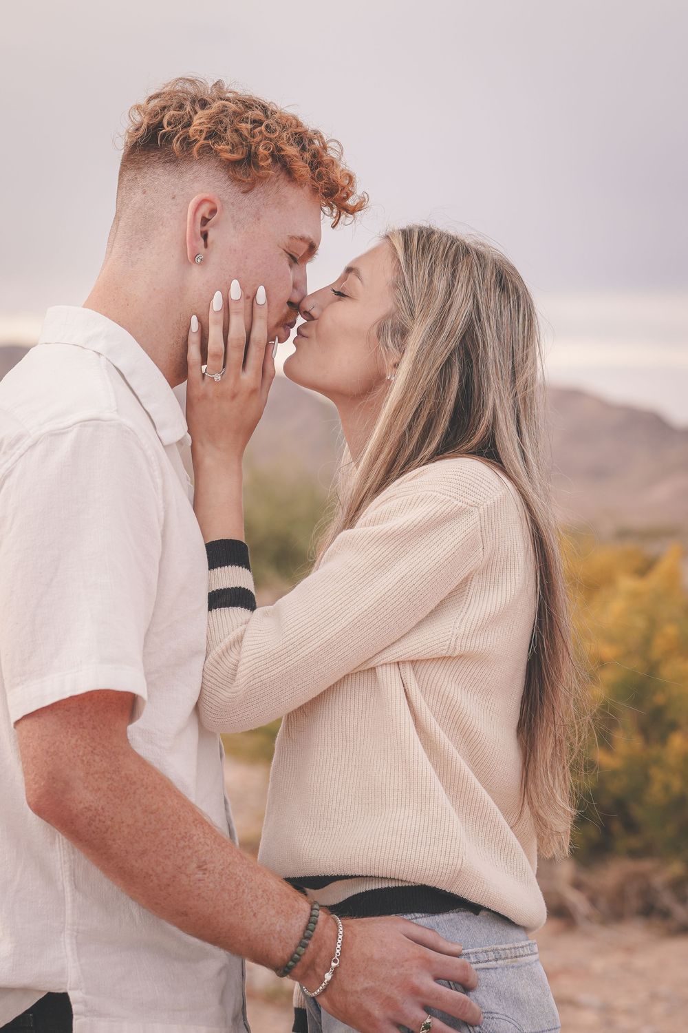 Young couple sharing a romantic almost-kiss outdoors, woman with manicured nails gently holding mans face.