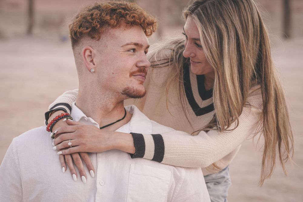 A young couple sharing a tender moment, smiling at each other outdoors in a warm, romantic embrace.