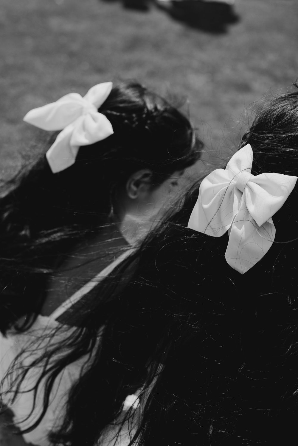 Two flower girls with white bow hair accessories photographed from above in black and white.